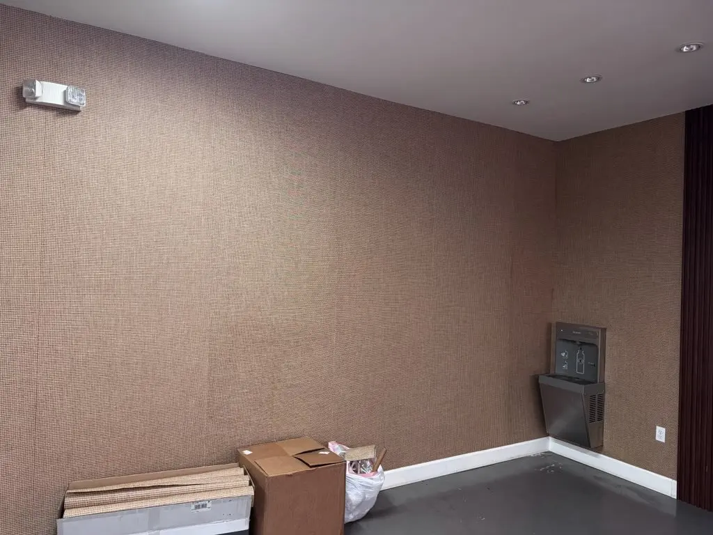 Quiet corner with warm taupe woven wallcovering, white baseboard, and cartons.