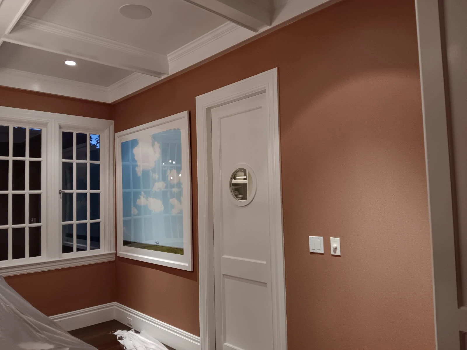 Warm muted mauve wallcovering framed by white trim, a paneled door, and a small round mirror.