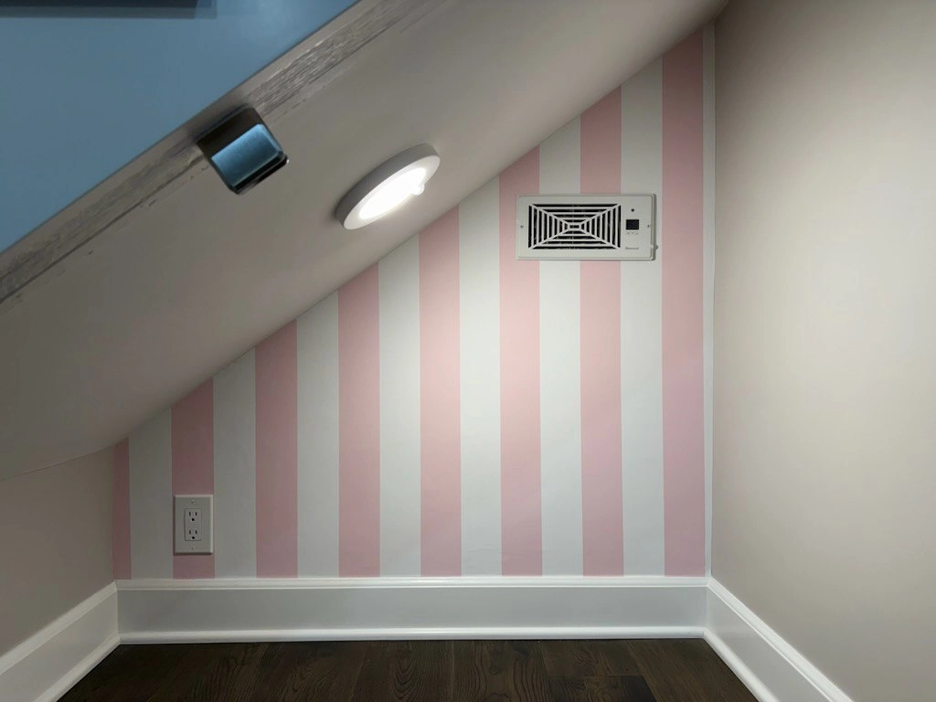 Small room with pale pink and white striped wallcovering beneath a sloped ceiling.